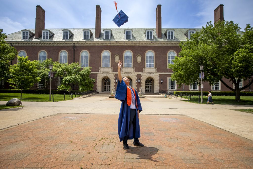 U of I graduate tosses cap in front of the Main Library.